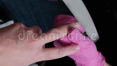 穿着粉红色手套的美甲师在美甲沙龙中用假指甲切割角质层和紫胶脚趾甲。 美容师的专业美甲